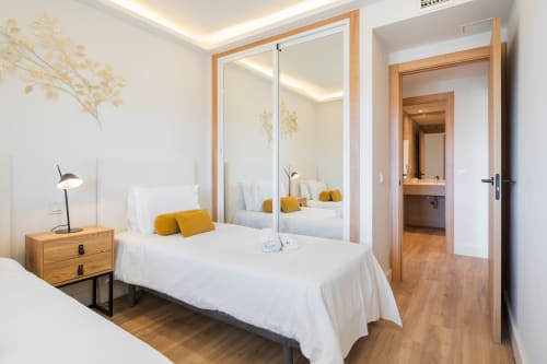 Modern bedroom at Marbella Home Rentals Marina Banús apartment with mirrored wardrobe, wooden nightstand, and yellow accent