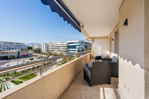 Spacious balcony with city views at Marina Banús apartment in Marbella, featuring seating area and modern amenities