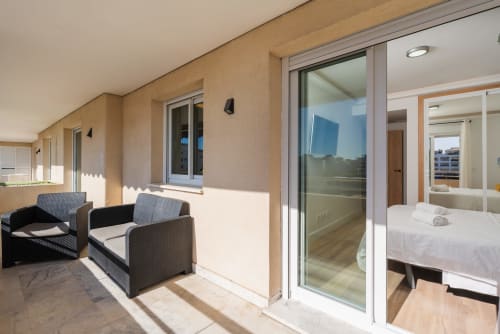 Sunny balcony with seating at Marbella Home Rentals 2-bedroom apartment in Puerto Banús, overlooking city views with modern