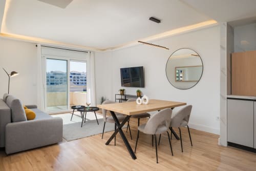 Modern Marbella apartment with dining table, gray sofa, round mirror, and balcony overlooking Puerto Banús city view