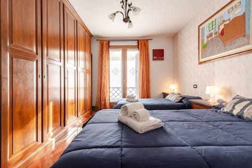 "Second bedroom at Casa Meravigliosa in Fontanafredda with two single beds, blue duvets, classic wooden bedside tables, and decorative paintings on the wall with light-colored wallpaper."