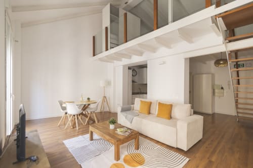 Moderno estudio en Málaga con cama alta, sofá crema, muebles de madera y sala abierta