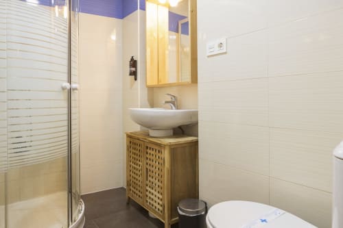 Baño moderno en el Ático Ab Be Málaga con azulejos blancos, lavamanos de madera, ducha, inodoro y techo azul