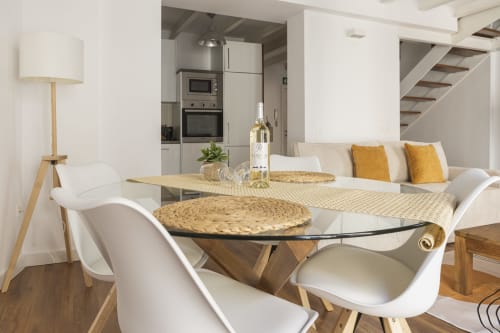 Elegante sala de comedor de ático con mesa de cristal, sillas blancas y vista a la cocina en apartamento de Málaga