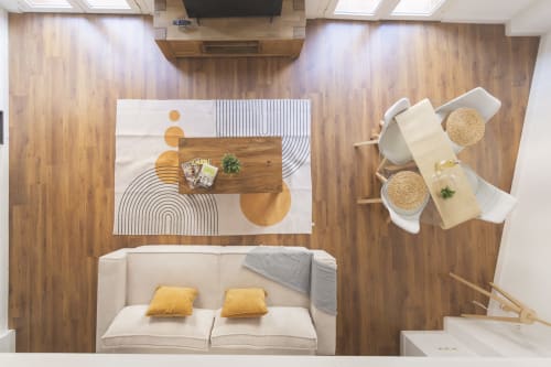 Vista aérea del Penthouse Ab Be en Málaga: sofá crema, mesa de madera, comedor y alfombras geométricas modernas