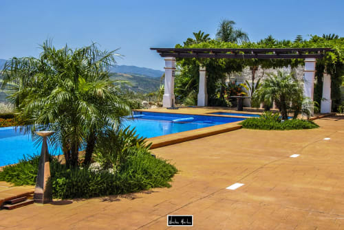 Luxurious Spanish hotel pool area with blue water, terracotta patio, palm trees, and pergola overlooking mountains