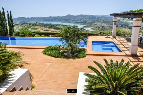 Luxury hotel terrace with blue pools, palm trees, and scenic lake and mountain views in Spain