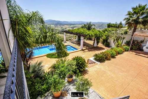 Luxury hotel courtyard with blue swimming pool, palm trees, terracotta patio, and mountain views in Spain