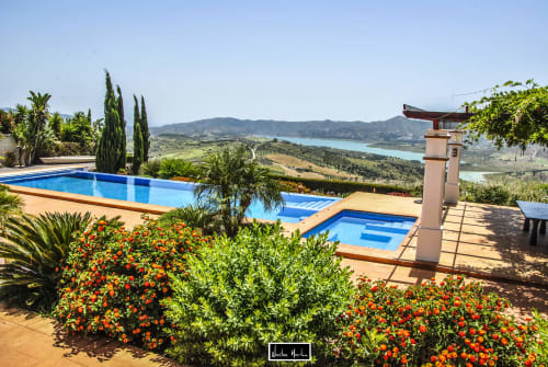 Luxury hotel pool overlooking turquoise lake and rolling hills in Spanish countryside with flowering gardens