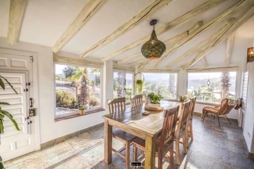 Bright sunroom dining area with wooden beams, dining table, and expansive windows overlooking gardens at Escanda Building