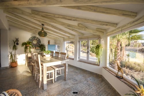 Bright dining room with wooden beams, large windows overlooking grounds, dining table, and potted plants at Escanda Building