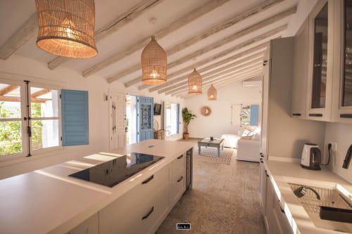 Modern open-plan kitchen with exposed beams, woven pendant lights, white cabinetry, and ocean views at Escanda hotel in Spain