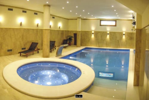 Indoor swimming pool and hot tub at Escanda Building Solutions hotel with lounge chairs and ambient lighting