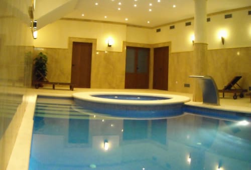 Indoor swimming pool at Escanda Building Solutions hotel with blue water, loungers, and warm lighting