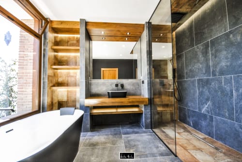 Modern luxury bathroom at Escanda Building Solutions hotel with dark slate tiles, wooden accents, soaking tub, and glass