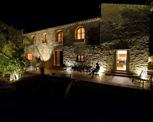 Patio de hotel de piedra iluminado por la noche con ventanas encendidas, arcos, muros cubiertos de hiedra y zona de descanso al aire libre en España
