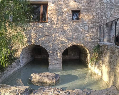 Historic stone building with arched water passages and ivy, Escanda hotel in Spain