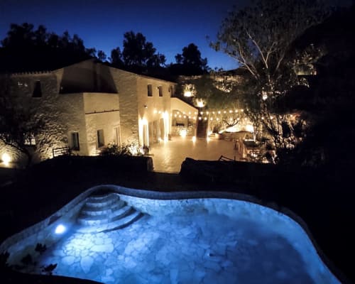 Illuminated Mediterranean villa at dusk with glowing pool and courtyard surrounded by trees in Spain