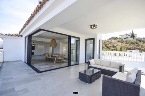 Modern hotel terrace with black-framed glass doors, rattan furniture, and hillside views in Spain