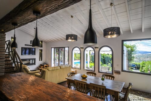 Modern luxury hotel interior with dining table, seating area, black pendant lights, and panoramic windows overlooking Spanish