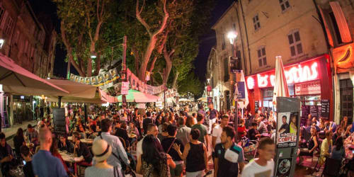 Lively evening street festival in Montfrin with crowds, outdoor dining, and illuminated trees near Le Prieuré Notre-Dame