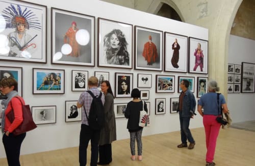Visitors viewing framed portrait gallery at Le Prieuré Notre-Dame in Montfrin featuring celebrity photographs and artwork