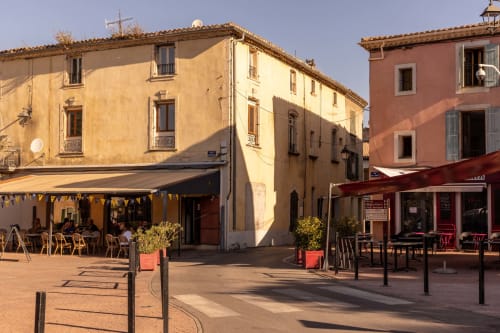 Sunny courtyard at Le Prieuré Notre-Dame in Montfrin with colorful buildings, outdoor seating, and dining areas