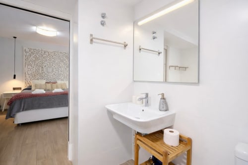 Baño moderno con lavabo blanco y estante de madera en apartamento Gestyp-AT, Mérida, con vista al dormitorio por puerta abierta
