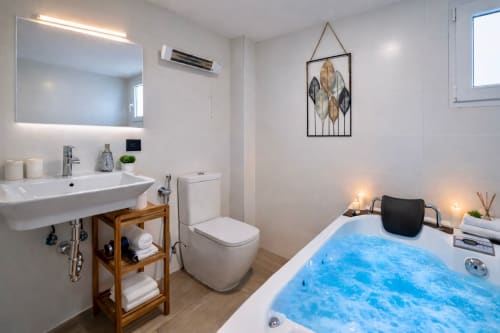 Baño moderno en apartamento de Mérida con espejo iluminado, tocador de madera, inodoro y jacuzzi con iluminación azul