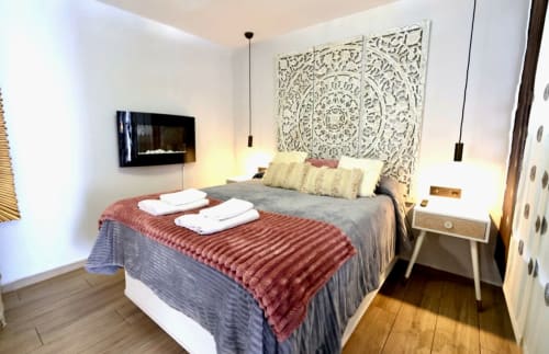 Recámara moderna en apartamento de Mérida con vista a la ciudad, cama con cabecera artística blanca, lámparas colgantes y piso de madera