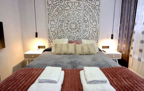Dormitorio moderno en apartamento Gestyp-AT en Mérida con cabecero blanco ornamentado, lámparas colgantes y vistas a la ciudad