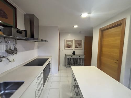 Cocina moderna en dúplex Lar de Mar, Baiona, con encimeras blancas, electrodomésticos acero inoxidable y puerta de madera