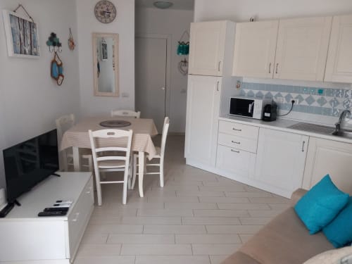Moderna zona cucina-soggiorno dell'appartamento Varenna by Foot con mobili bianchi, tavolo da pranzo, TV e dettagli turchesi
