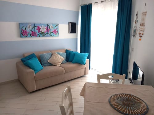 Soggiorno moderno a Varenna con divano beige, cuscini teal, pareti righe e accesso al balcone
