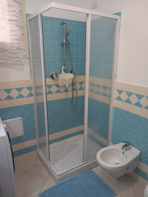 Bagno moderno con doccia in piastrelle turchesi, bidet e dettagli geometrici blu nell'appartamento Varenna by Foot in Italia