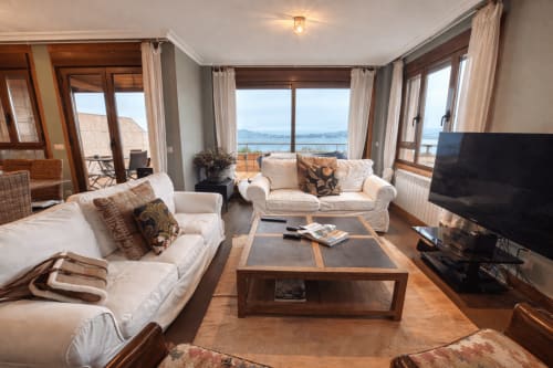 Luminoso apartamento en Baiona con sofás crema, mesa de café de madera, ventanas con vistas al océano y TV de pantalla plana