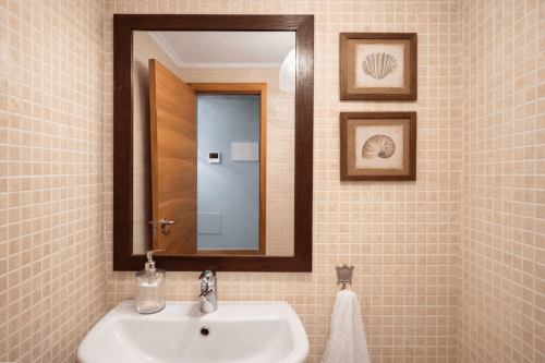 Baño moderno con paredes alicatadas, espejo de marco de madera oscura, lavamanos blanco y decoración costera en el apartamento Lar de Mar