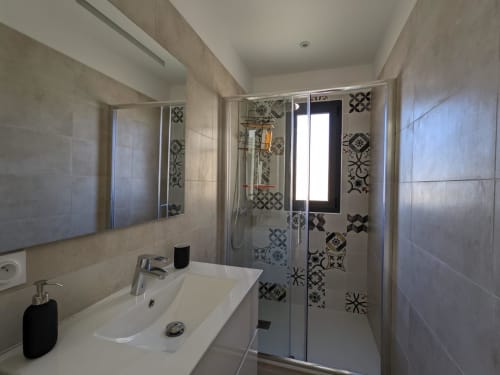 Modern bathroom with white sink, mirror, and black and white patterned shower enclosure at Villa Ô Bord de Mer, Corsica, managed by Corsu di Core