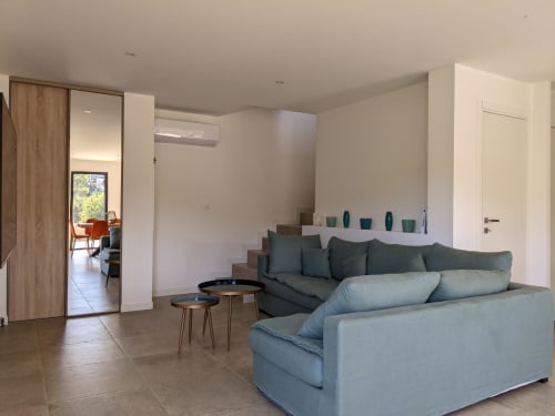 Modern villa living room with grey sofas, wooden door, white walls, and pool view at O Bord de Mer villa, Favone, managed by Corsu di Core