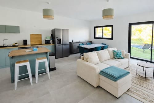 Modern open-plan villa at Corsu Di Core with equipped kitchen, cream sofa, dining area, and pool view through glass doors, managed by Corsu di Core conciergerie