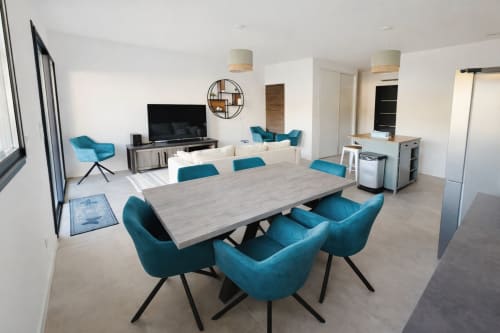 Modern villa dining area with teal chairs, wood table, kitchen, TV lounge, managed by Corsu di Core conciergerie