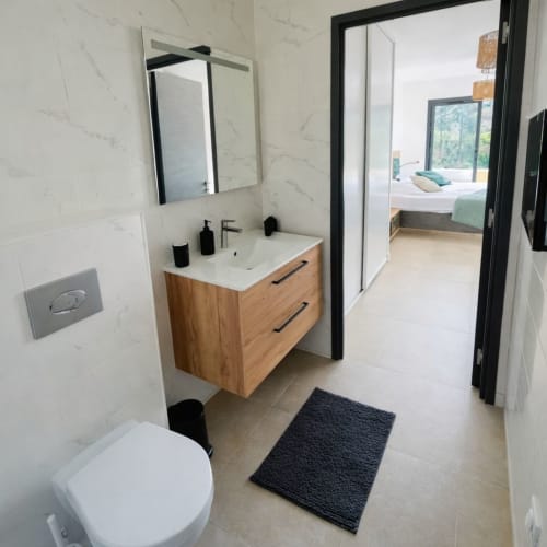 Modern bathroom in Villa Lagon Bleu at  Favone with wooden vanity, white sink, mirror, and toilet, managed by Corsu di Core