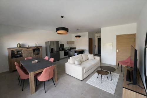 Open-plan living area in Villa Corail at Corsu Di Core with cream sofa, dining table, pink chairs, and modern kitchen, managed by Corsu di Core