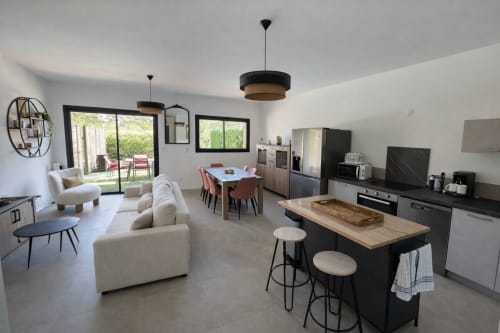 Modern open-plan living area in Villa Corail  with kitchen, dining table, cream sofa, and garden, managed by Corsu di Core