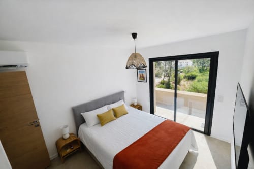 Bright modern bedroom in Villa Corail at  with queen bed, garden view doors, and woven pendant light managed by Corsu di Core
