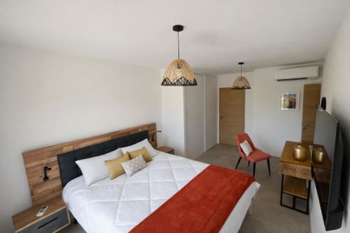 Modern bedroom in Villa Corail with wooden bed, woven pendant lights, and red accent chair, managed by Corsu di Core