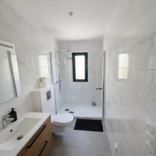 Modern bathroom in Villa Corail , white tile walls, wooden vanity, glass shower enclosure, toilet, managed by Corsu di Core