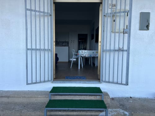 Cancellate metalliche bianche aperte rivelano l'ingresso dell'appartamento arredato della proprietà fronte mare Lux Immobiliare a Marina di Strongoli,