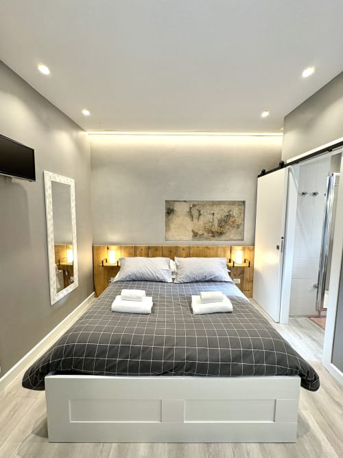 Camera moderna a Le Arche Verona con letto matrimoniale, testiera in legno, bagno en suite e illuminazione ambientale