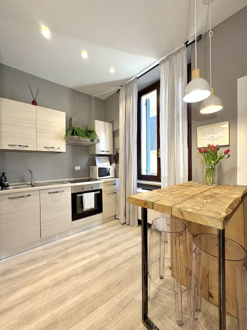 Cucina moderna e zona pranzo nell'appartamento di Verona con mobili bianchi, tavolo in legno e accesso al balcone con vista sulla città.